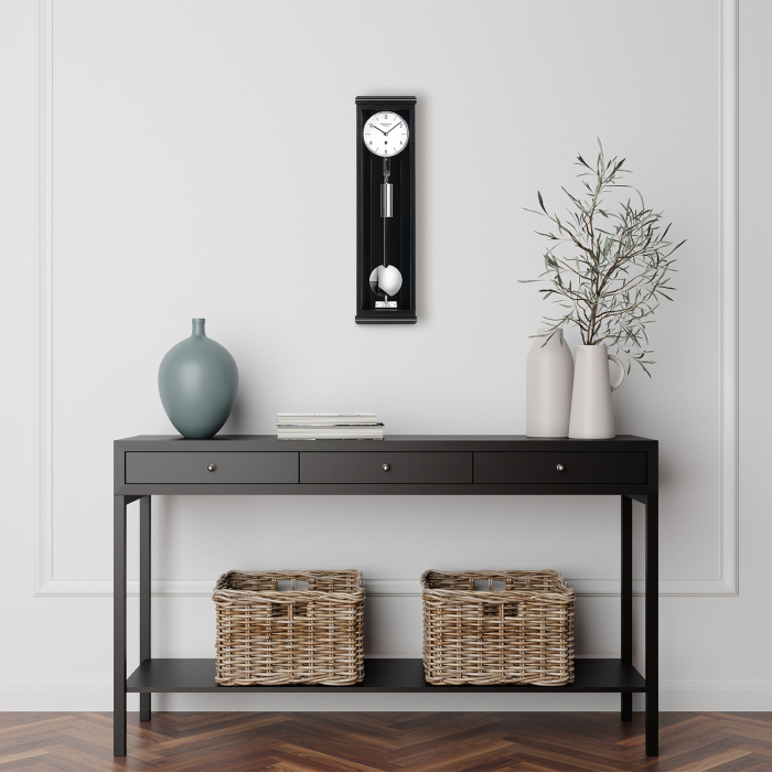 Moderne Wohnzimmer-Szene mit Erwin Sattler Wanduhr Classica S 60 M in schwarzem Gehäuse an weißer Wand