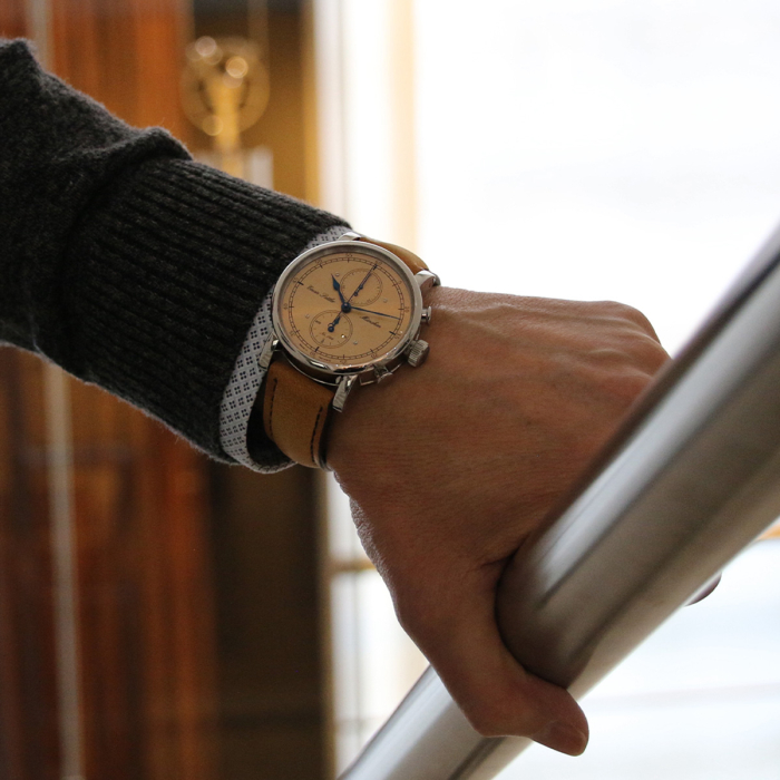Armbanduhr Erwin Sattler Chronograph mit kupferfarbenem Zifferblatt am Handgelenk, getragen an einem Treppengeländer