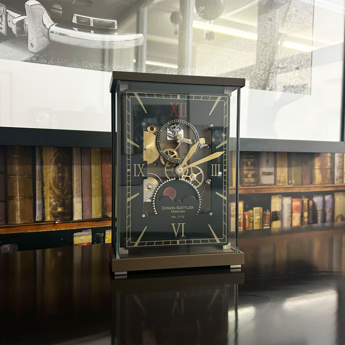 Lunaris Sanguis Tischuhr von Erwin Sattler auf einem Schreibtisch vor Bücherregal, mechanisches Uhrwerk sichtbar